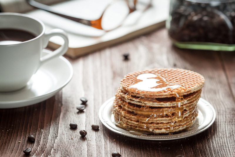 Uma pilha do típico doce holandês o Stroopwafel, escorrendo caramelo, com café.